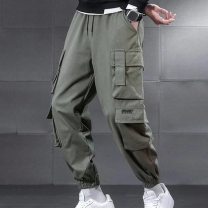 Green cargo pants worn by a person on a gray tiled wall background